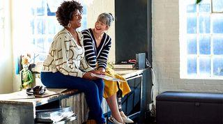 Two women sitting on top of a sideboard laughing